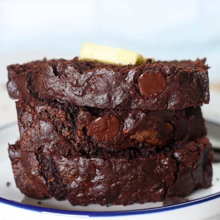 Double chocolate zucchini bread slices stacked on a plate with a pat of butter on top.