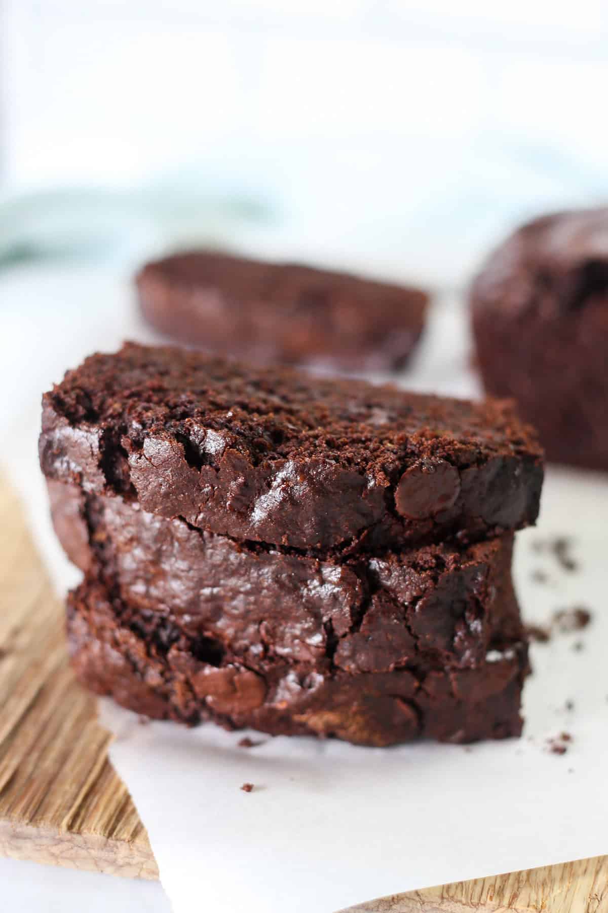 Three slices of double chocolate zucchini bread stacked up on parchment paper.