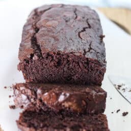Double chocolate zucchini bread on a wooden cutting board with half of it in slices.