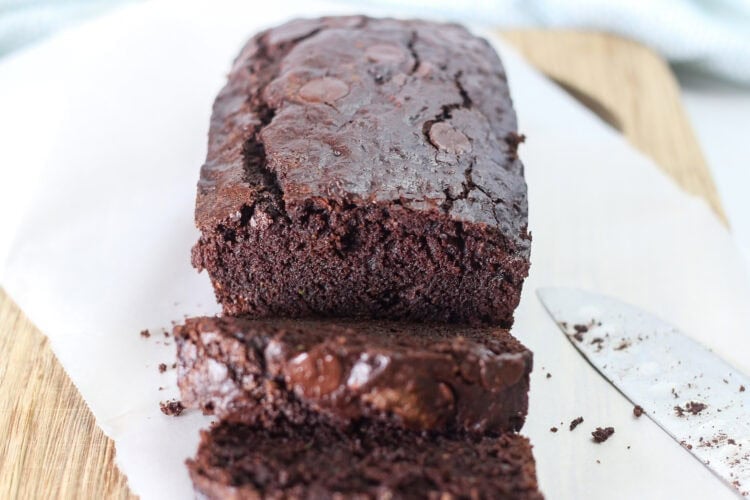 Double chocolate zucchini bread on a wooden cutting board with half of it in slices.