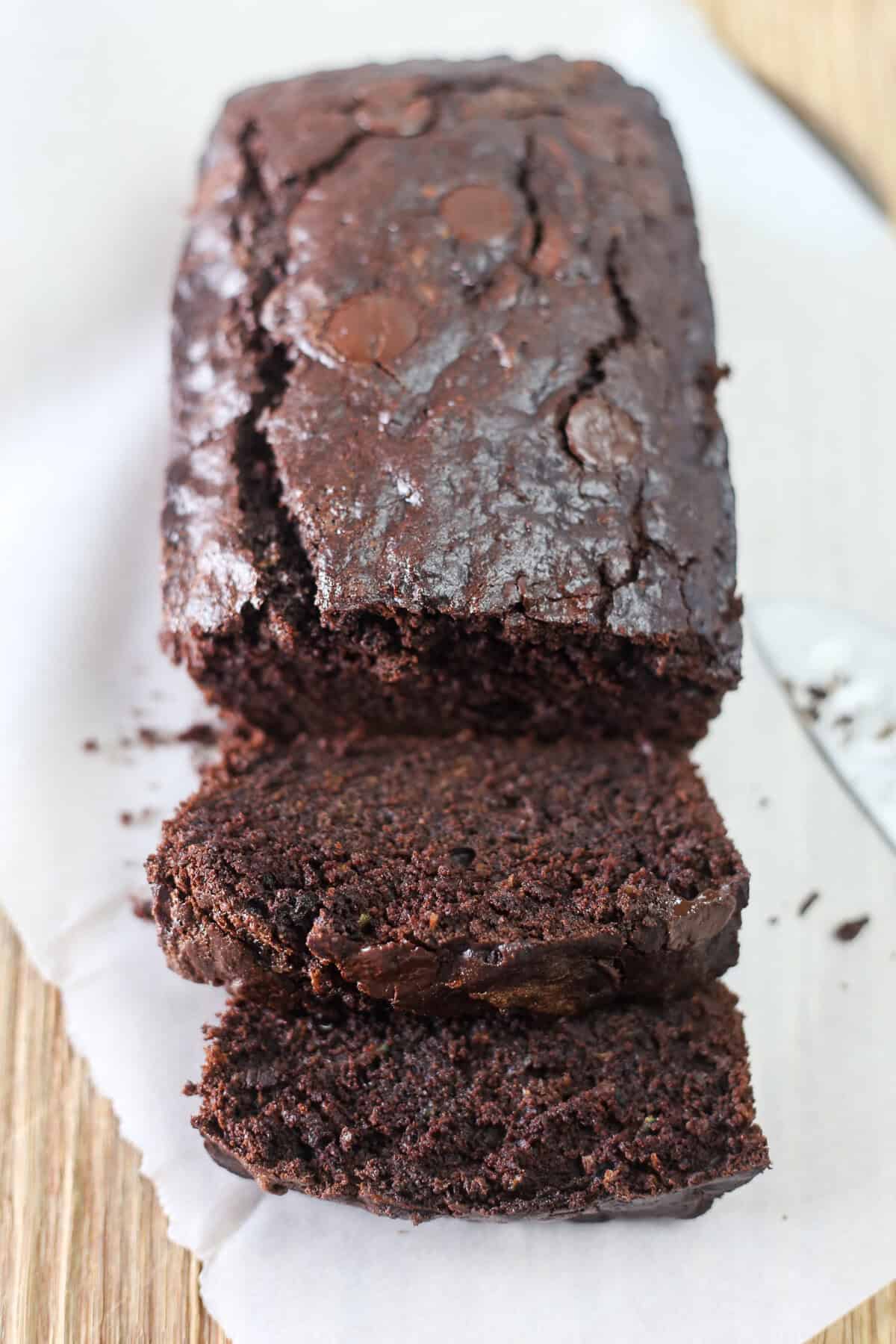 Double chocolate zucchini bread on parchment paper with half of it sliced.