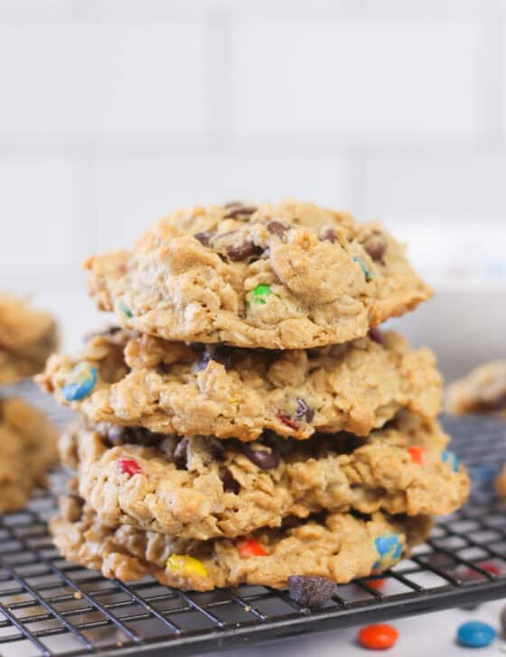 Stacked monster cookies on a black cooling rack with oats and m&m's sprinkled around.