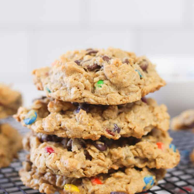 Stacked monster cookies on a black cooling rack with oats and m&m's sprinkled around.