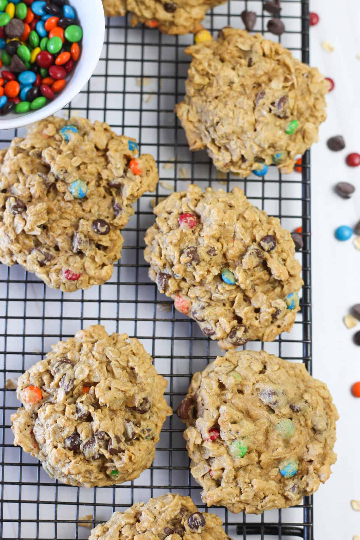 Monster cookies on a black cooling rack with M&Ms spread around. 