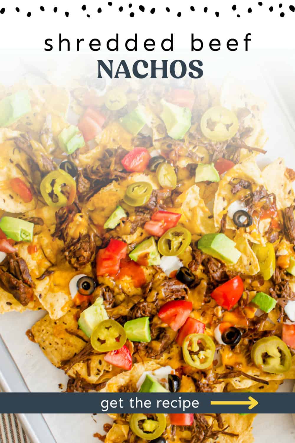 Shredded beef nachos on a baking sheet with toppings on it ready to serve.