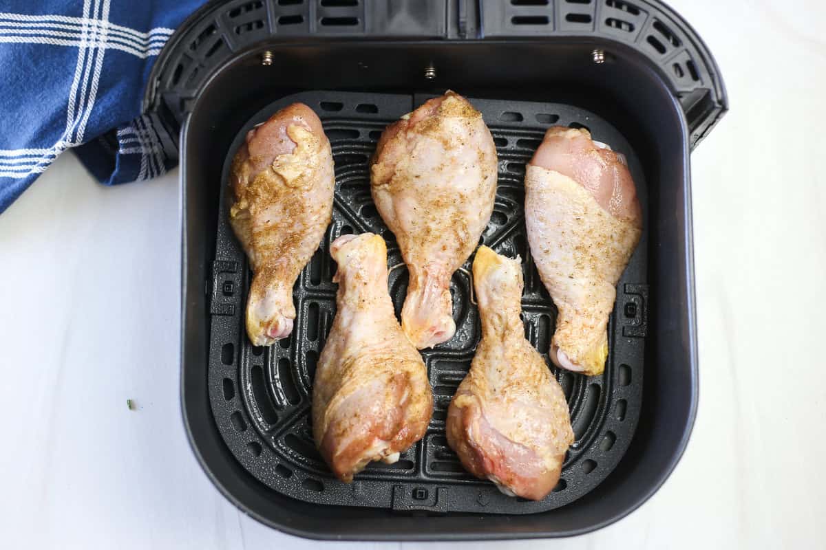 Seasoned chicken drumsticks arranged in an air fryer basket ready to cook.
