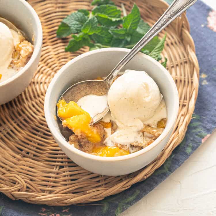 A serving of peach cobbler in a white bowl with ice cream on top.