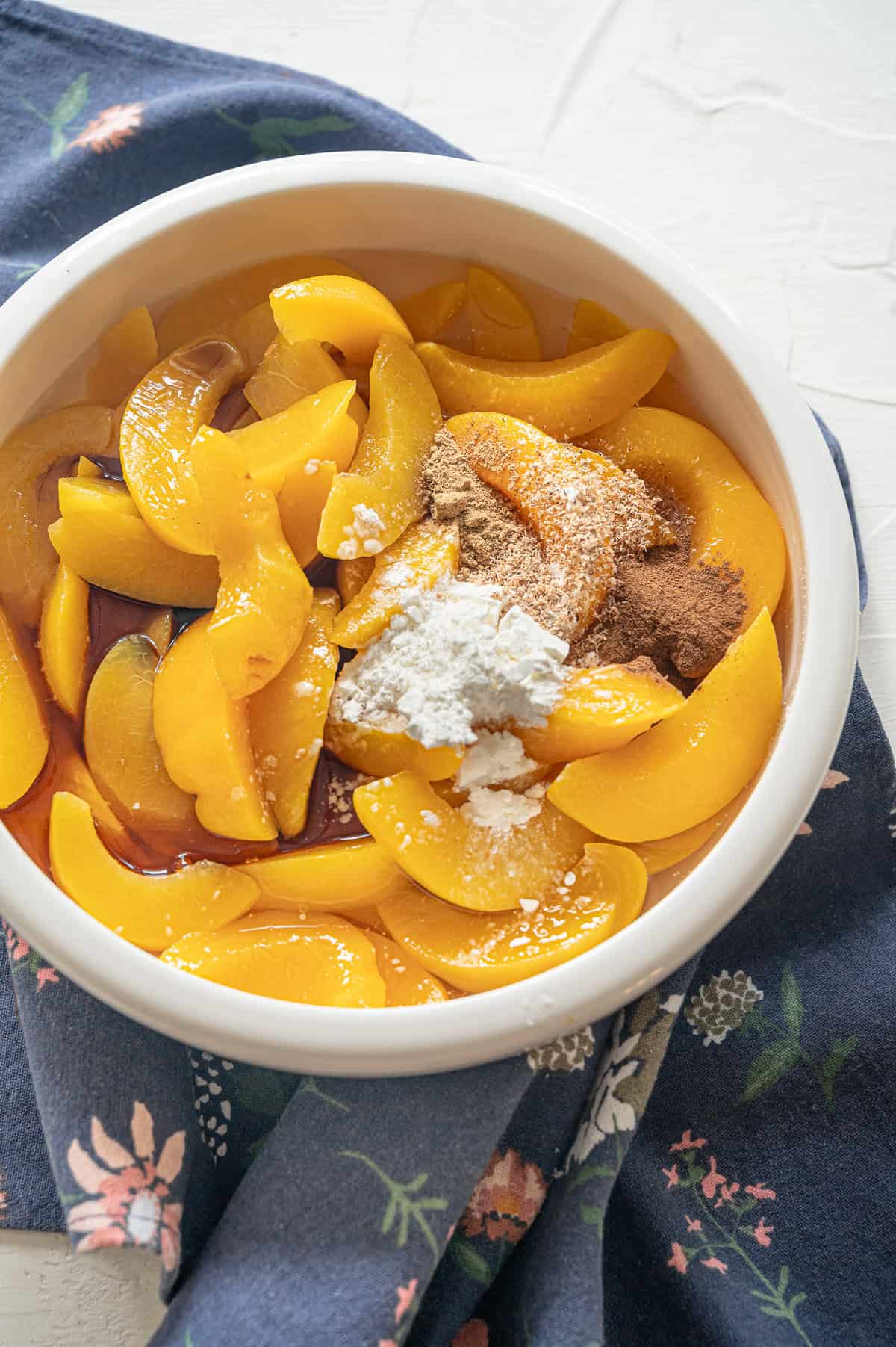 Canned peaches in a bowl with cornstarch and spices on top ready to mix in.