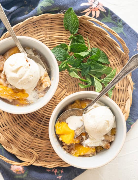 Two bowls of peach cobbler with ice cream on top and fresh mint next to them.