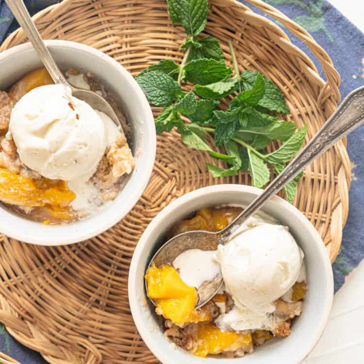 Two bowls of peach cobbler with ice cream on top and fresh mint next to them.