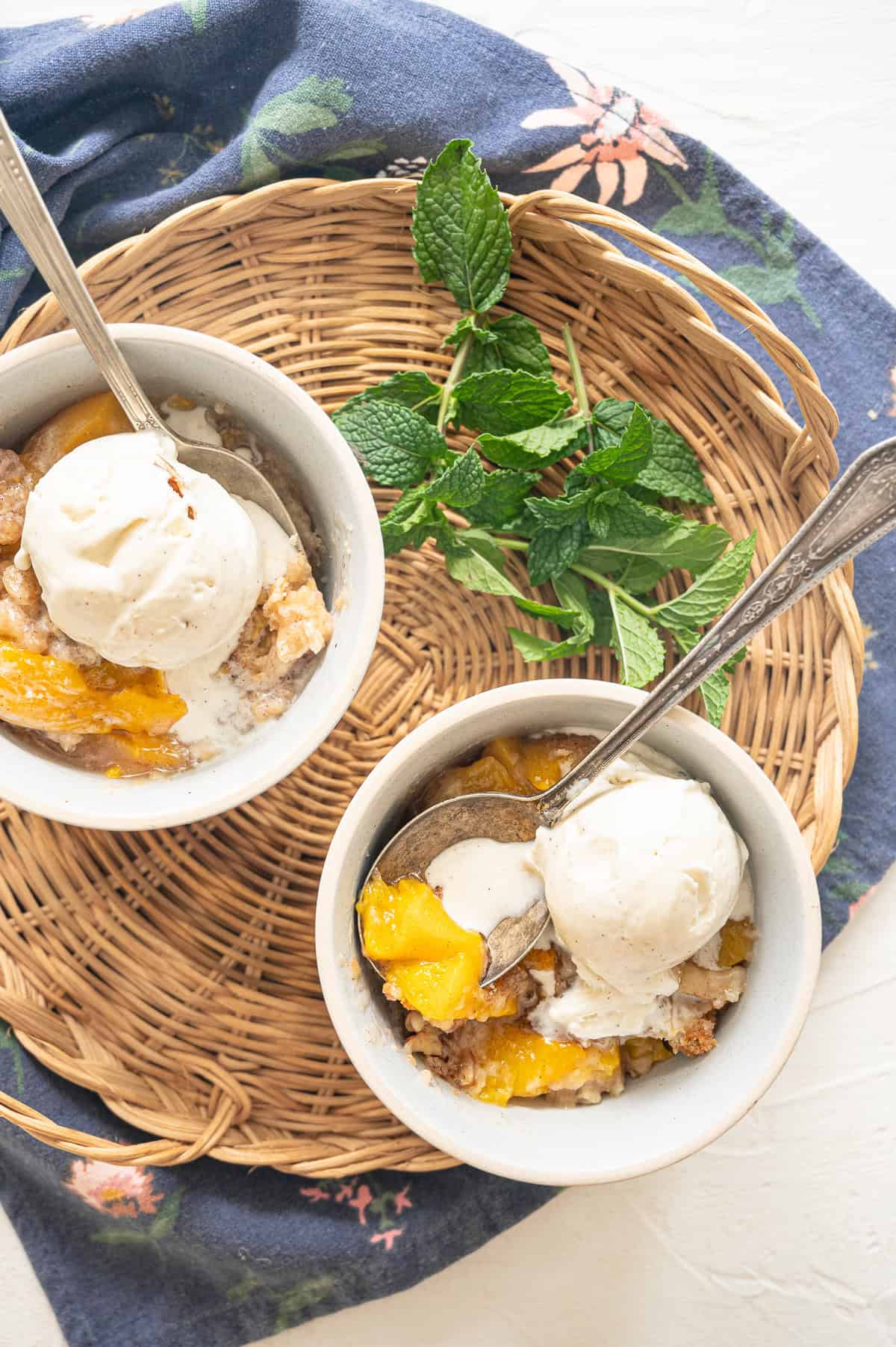 Two bowls of peach cobbler with ice cream on top and fresh mint next to them.