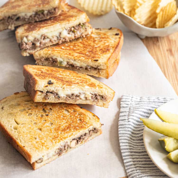 Ground beef Philly cheesesteak sandwiches cut in half and stacked up so you can see the cheese melting out.