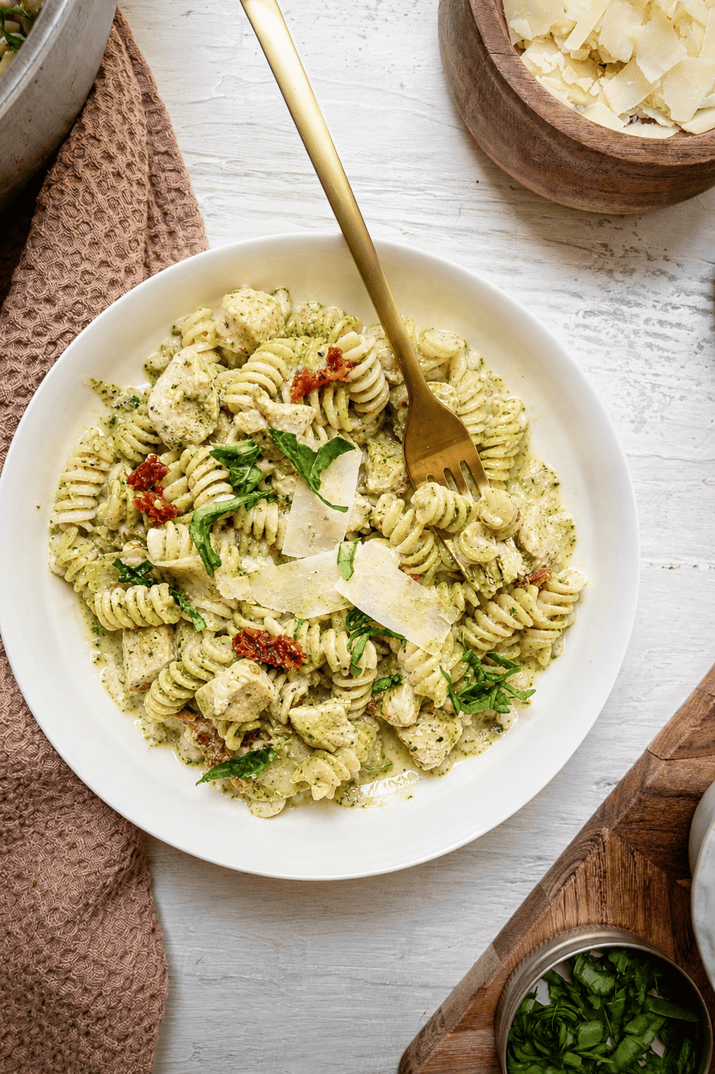 A plate of creamy chicken pesto pasta on a white plate with a fork.