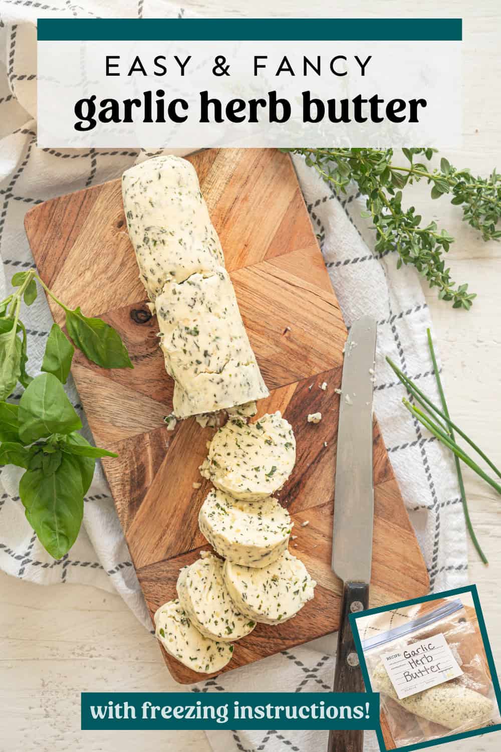 A log of garlic herb butter on a cutting board with some of it sliced and fresh herbs around it.