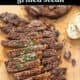 Grilled steak that's been sliced on a cutting board and has garlic herb butter on top.