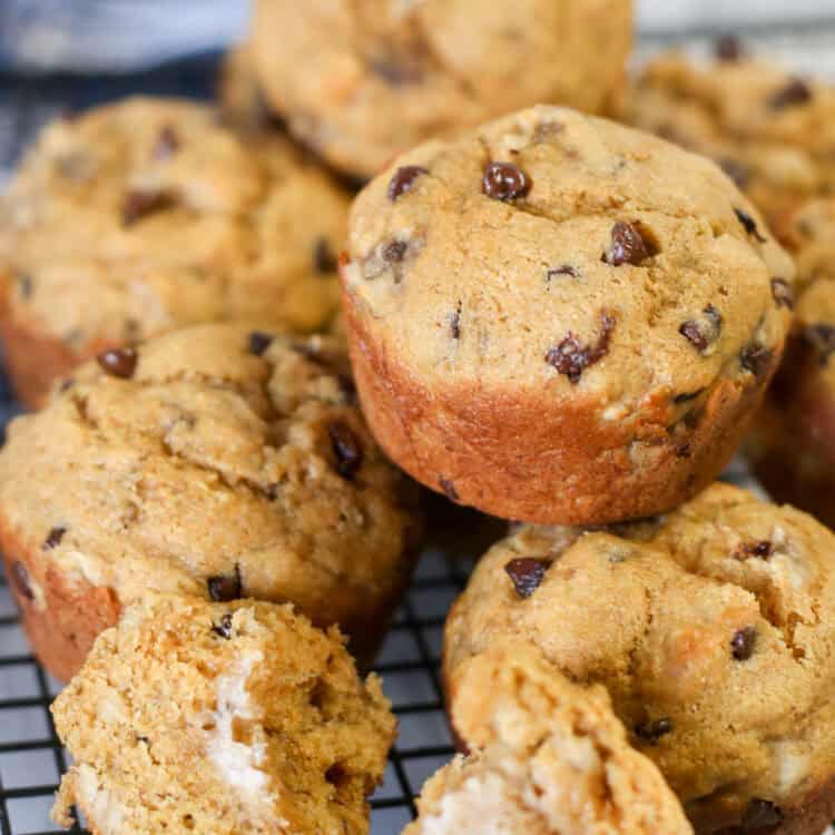 A pile of healthy chocolate chip banana muffins with one muffins split open and buttered.