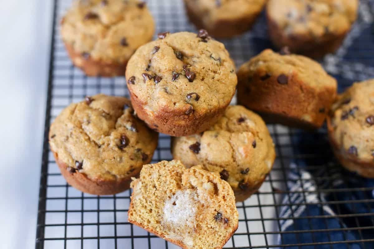 A pile of healthy chocolate chip banana muffins with one muffins split open and buttered.