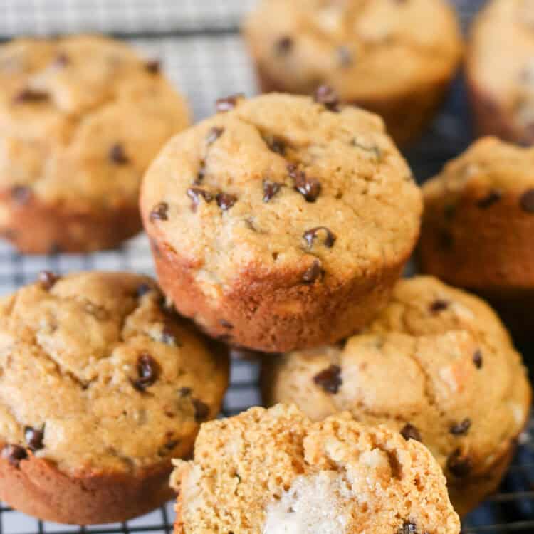 A pile of healthy chocolate chip banana muffins with one muffins split open and buttered.