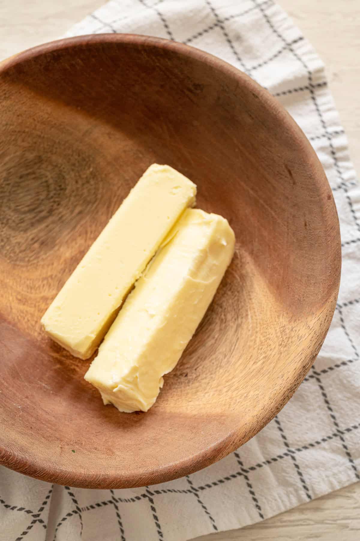 Two softened sticks of butter in a wooden bowl.