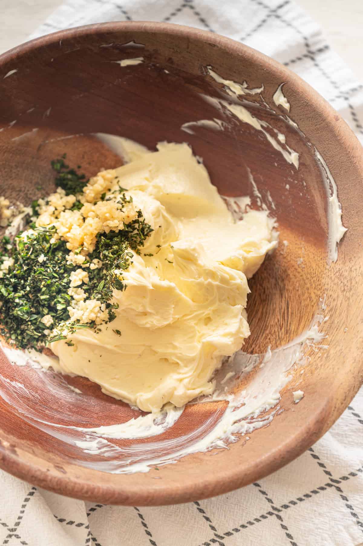 Whipped butter in a wooden bowl with minced garlic and fresh chopped herbs dumped in ready to mix.