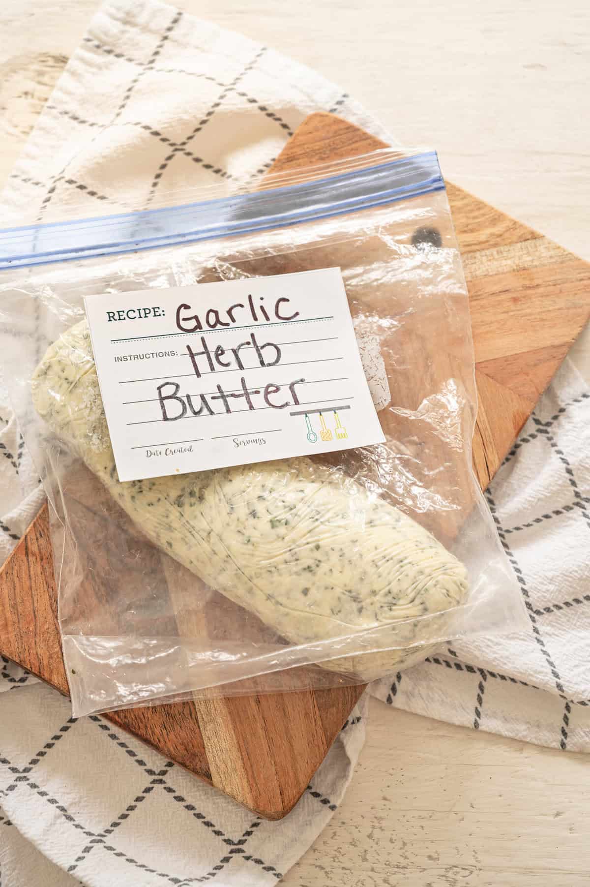 Roll of butter wrapped in plastic wrap inside a freezer-safe bag labeled Garlic Herb Butter.