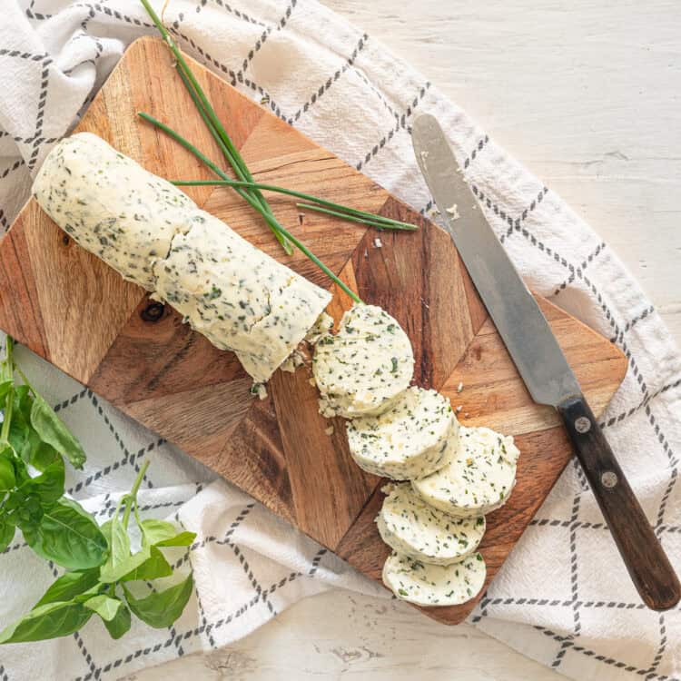 A roll of garlic herb butter on a cutting board with part of it already sliced for serving.