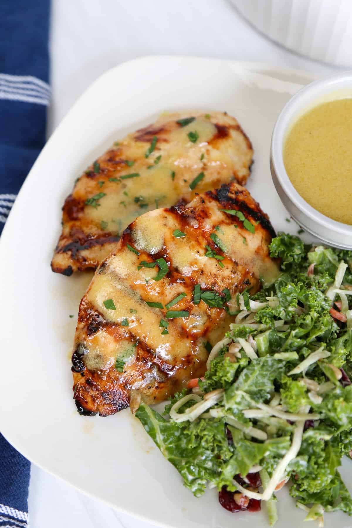 Honey Dijon grilled chicken breasts with salad and a small container of honey Dijon dipping sauce.