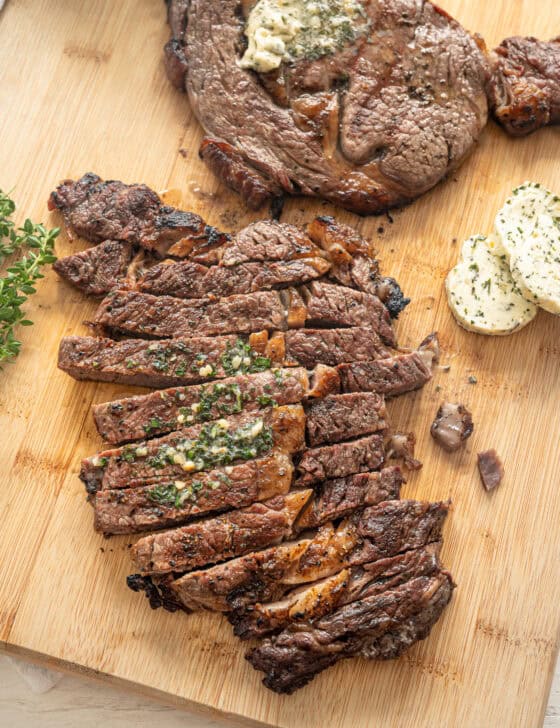 Sliced grilled steak on a cutting board with another steak behind it waiting to be cut.