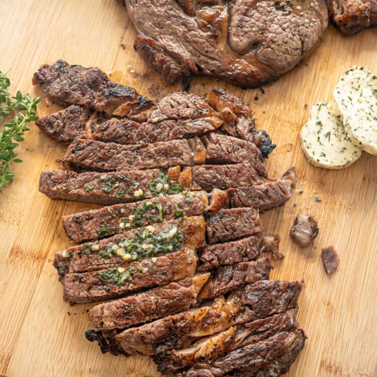 Sliced grilled steak on a cutting board with another steak behind it waiting to be cut.