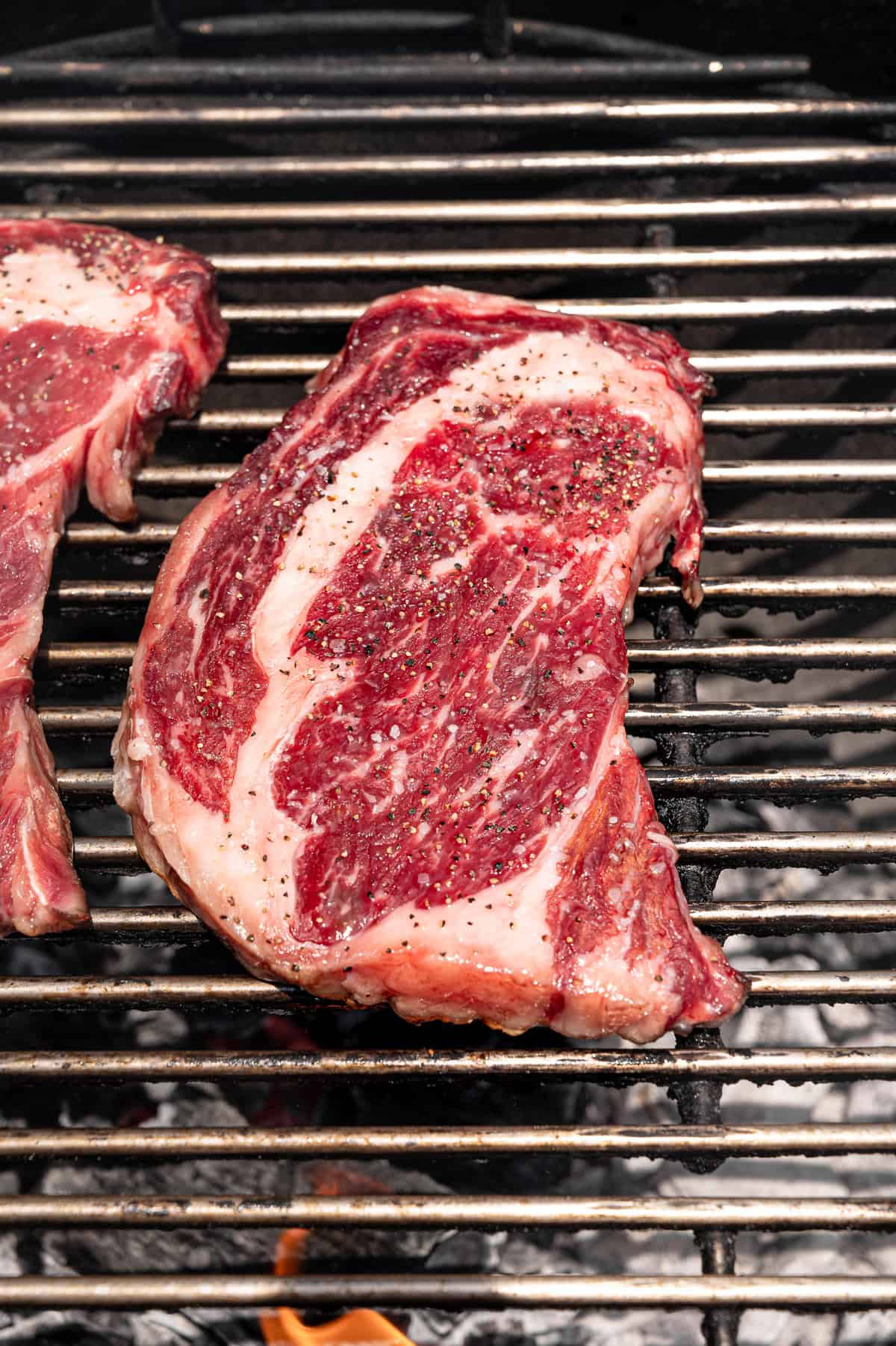 A steak with salt and pepper on a grill.