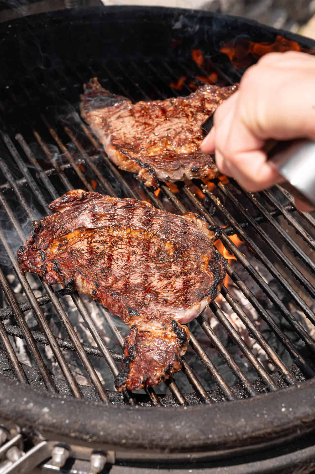 A hand using tongs to flip a steak on a grill.