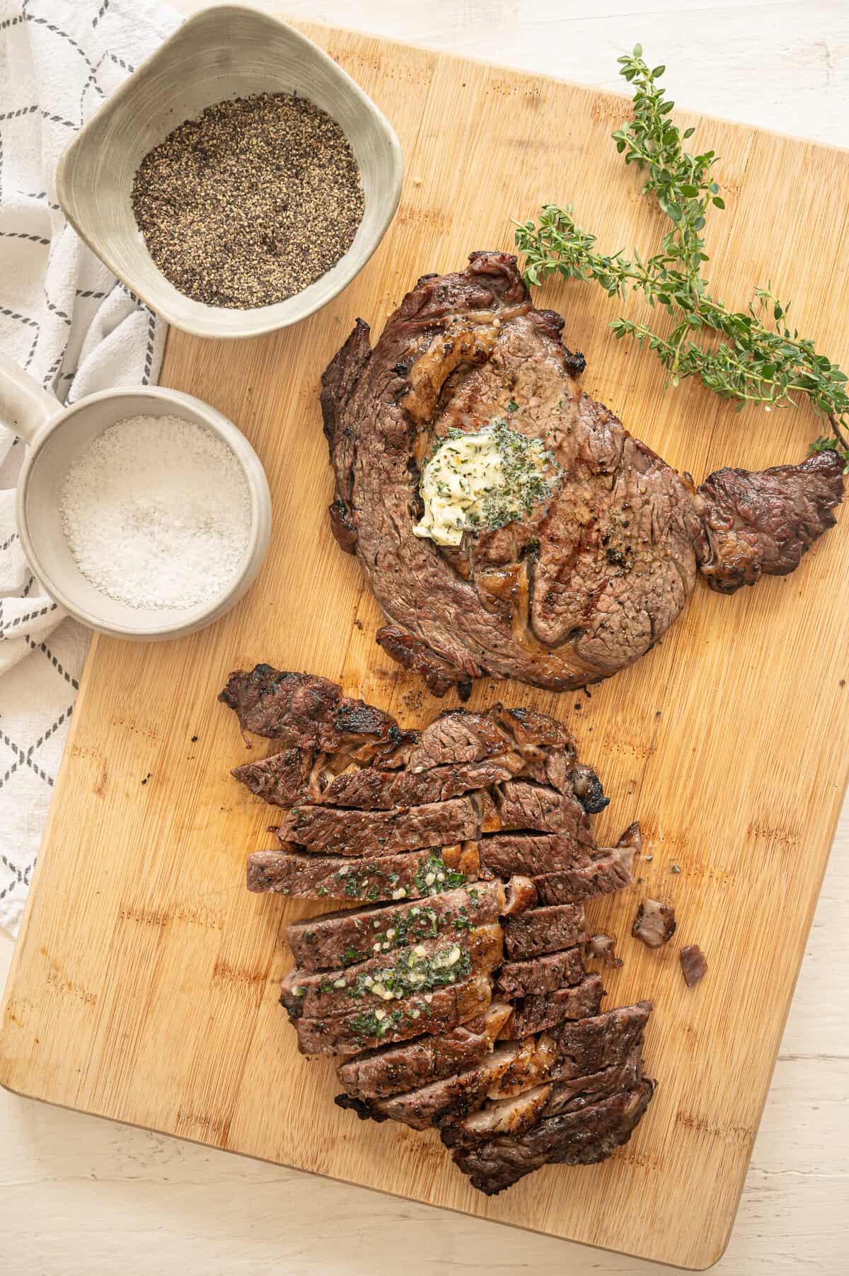 Two steaks on a cutting board, one sliced and the other with garlic herb butter on top.