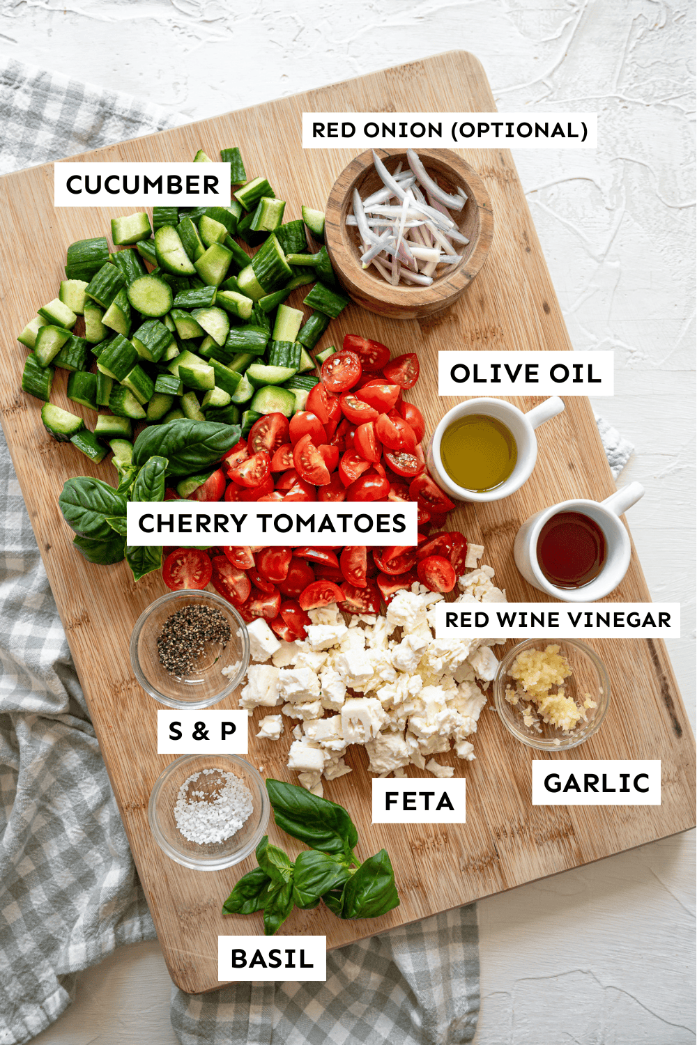 A wooden cutting board with various ingredients on it like chopped cucumber, cherry tomatoes, feta, garlic, and more.