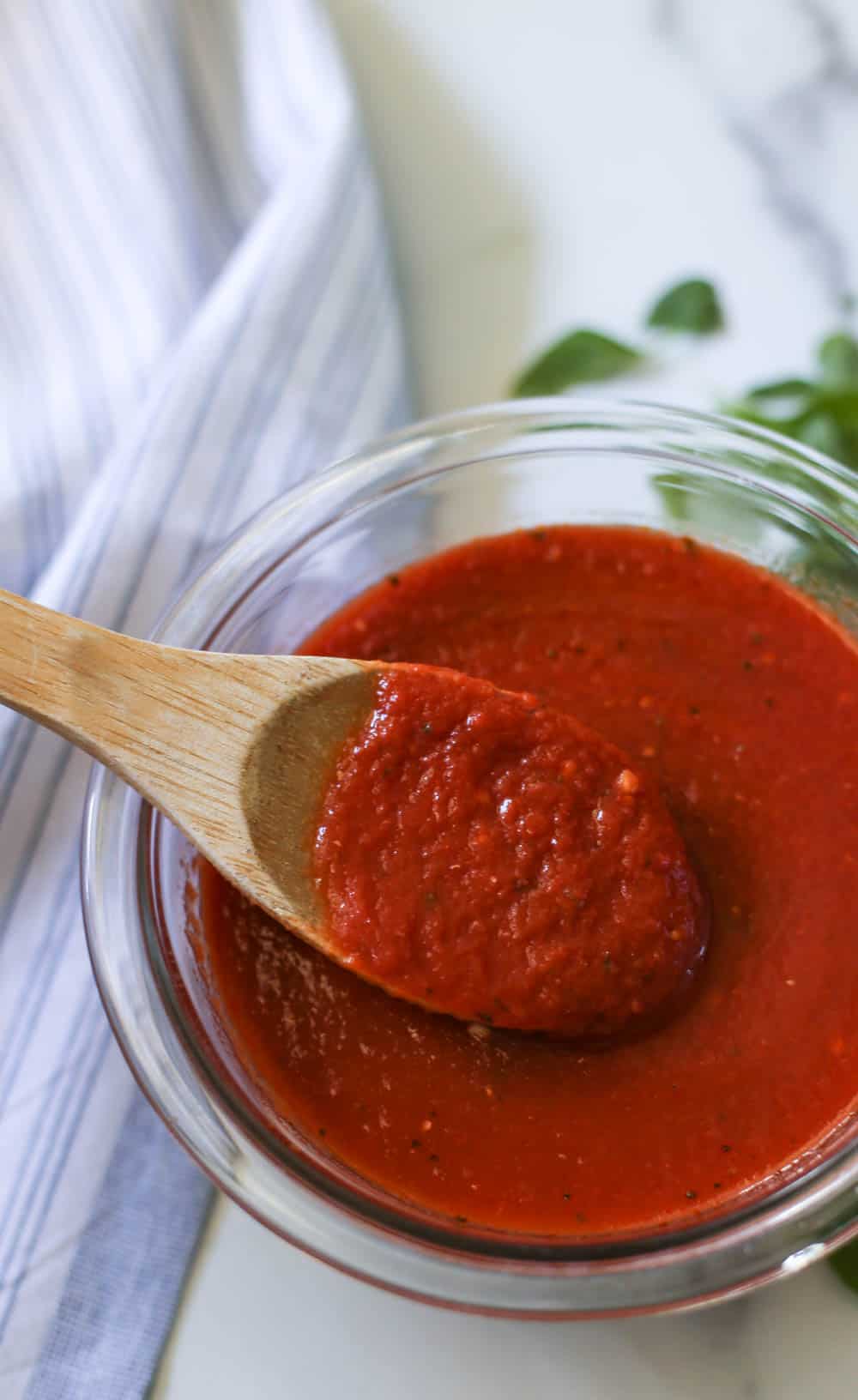 A bowl of homemade pizza sauce with a wooden spoon dipped into it. 