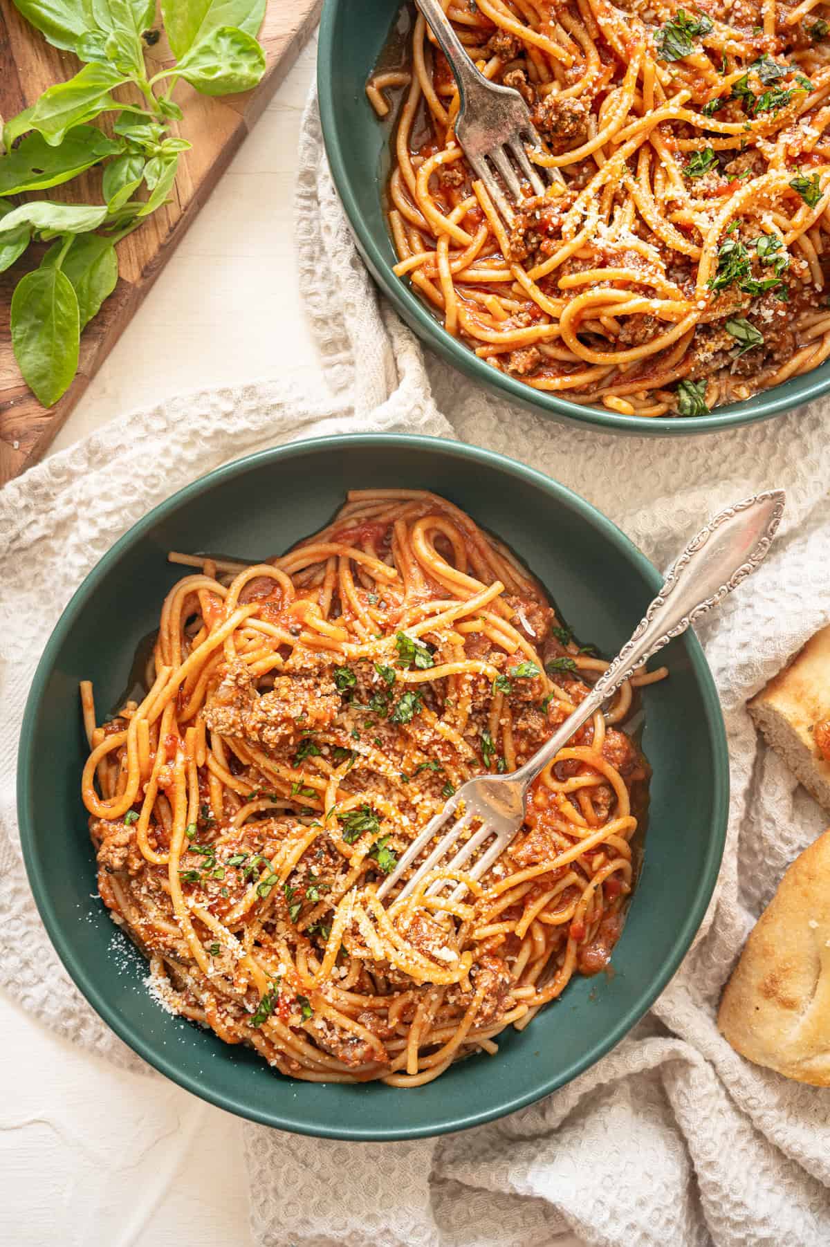 Instant Pot spaghetti with meat in bowls with fresh basil on the side.