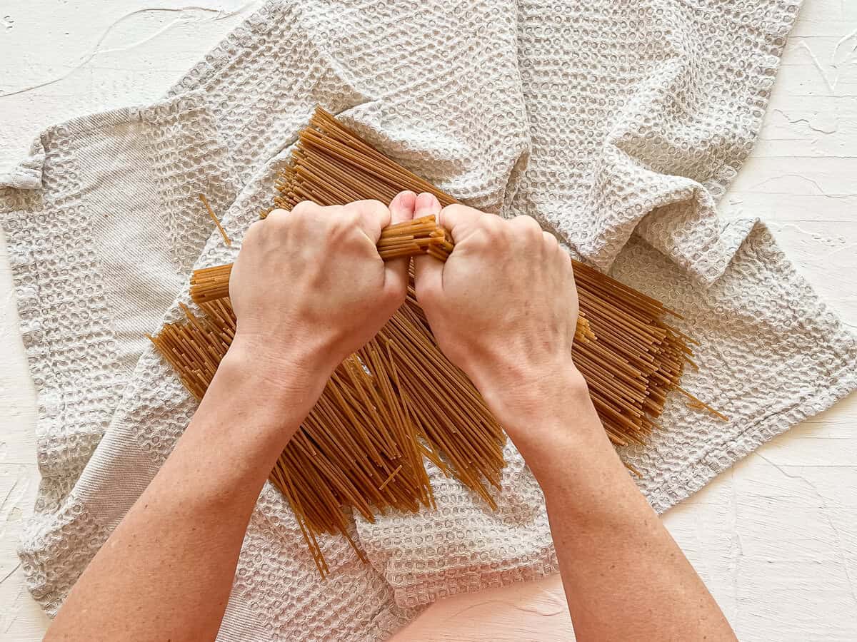 Two hands breaking whole wheat spaghetti noodles in half to fit in an Instant Pot.