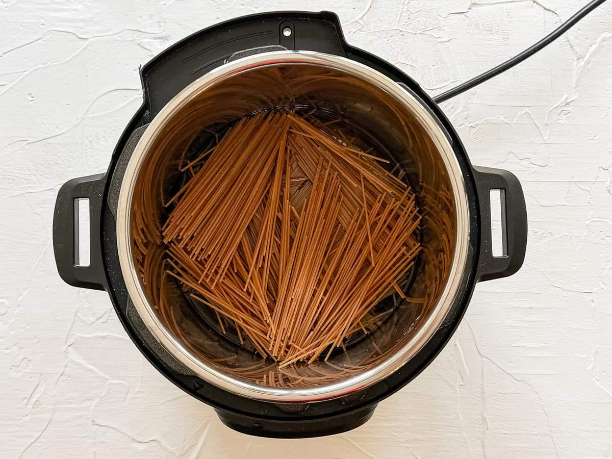 Uncooked whole wheat spaghetti noodles in water in an Instant Pot.