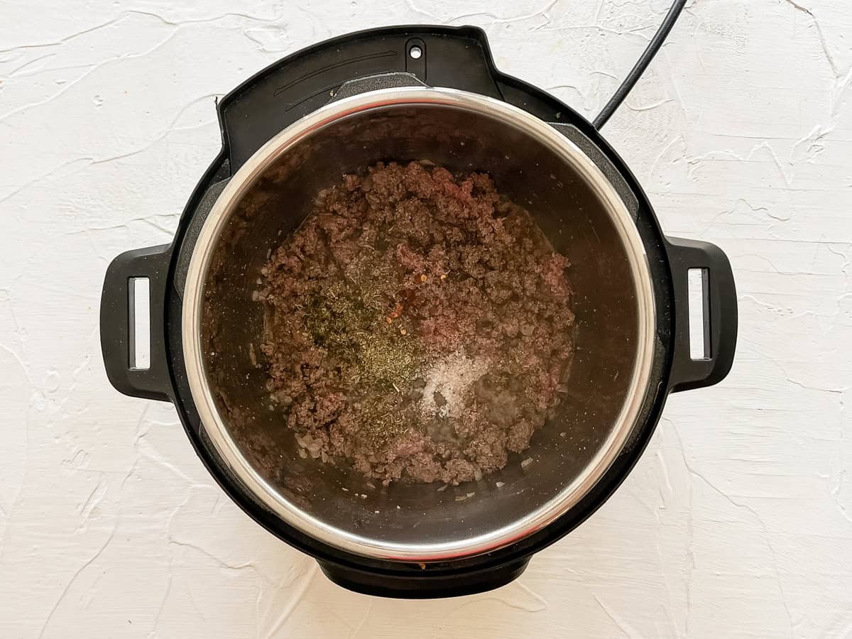 Ground beef sauteeing in the Instant Pot with seasonings on top.