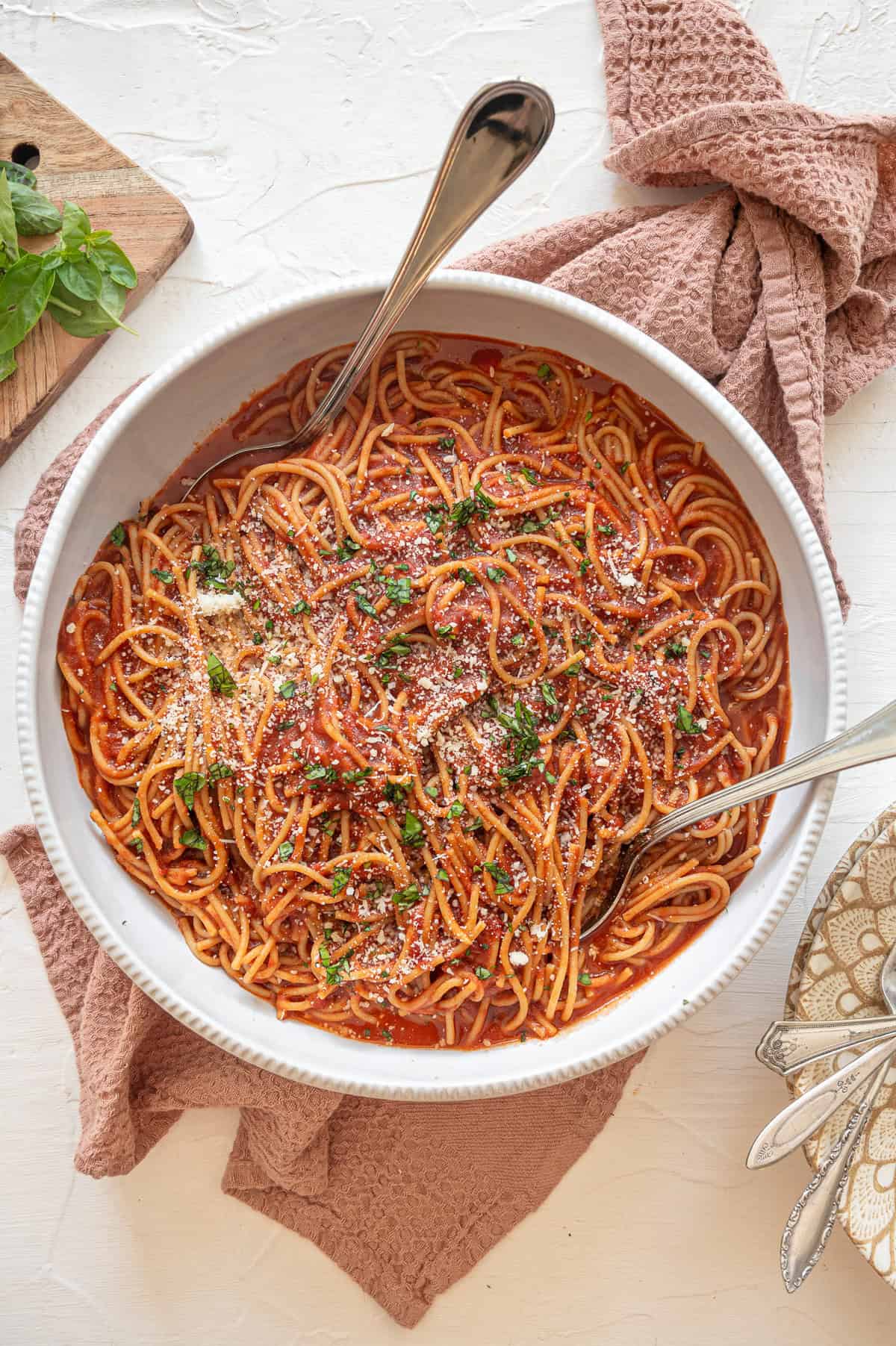 Large white bowl of Instant Pot spaghetti with chopped basil and grated Parmesan cheese on top.