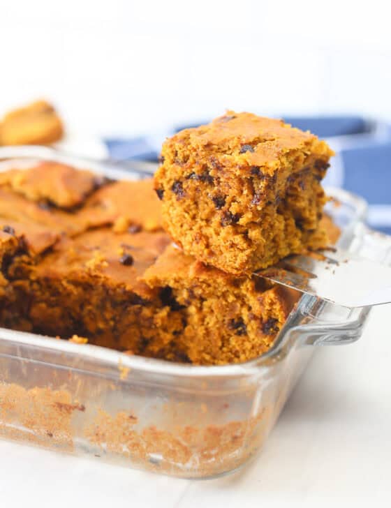 A spatula holding a piece of banana breakfast cake above the square baking dish it came out of.