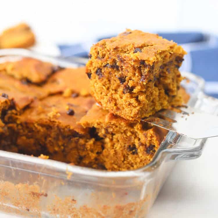 A spatula holding a piece of banana breakfast cake above the square baking dish it came out of.