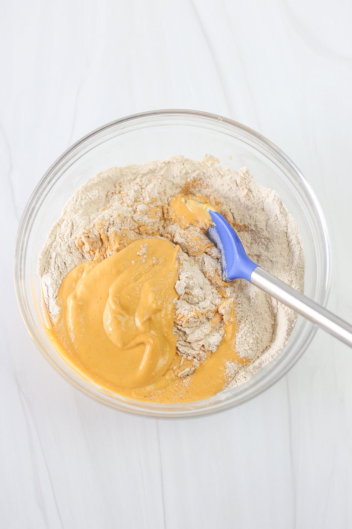 A glass bowl with a spoon mixing together wet and dry ingredients for banana breakfast cake.