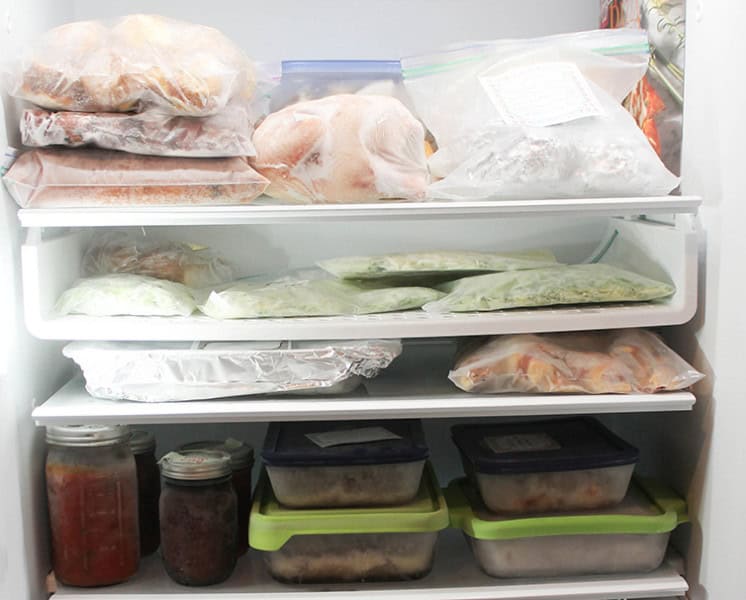 Looking inside a freezer with meals packaged in a variety of ways including mason jars, freezer bags, and glass baking dishes with lids. 