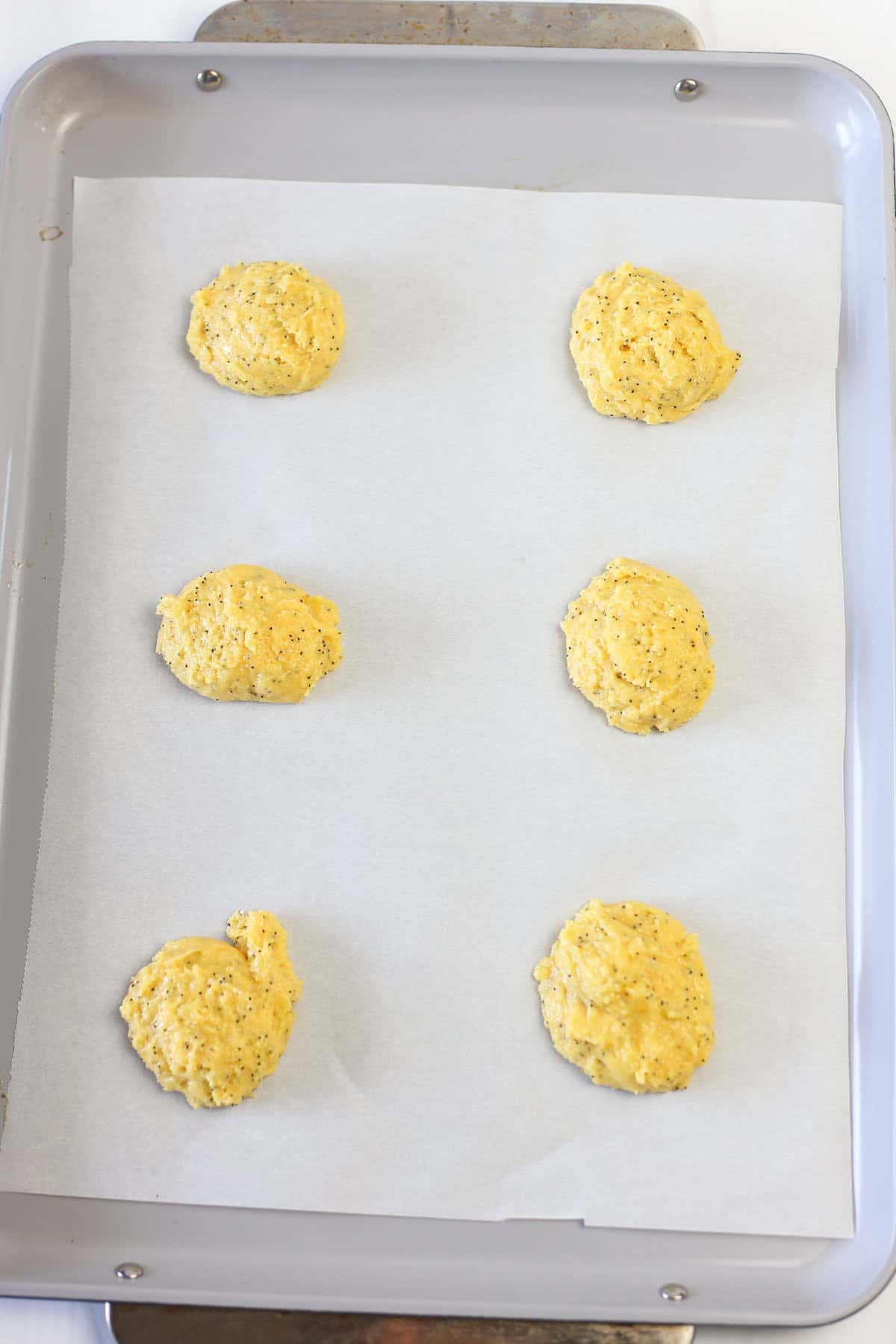 Lemon poppyseed cake mix cookie dough on a parchment paper lined baking sheet ready for the oven.