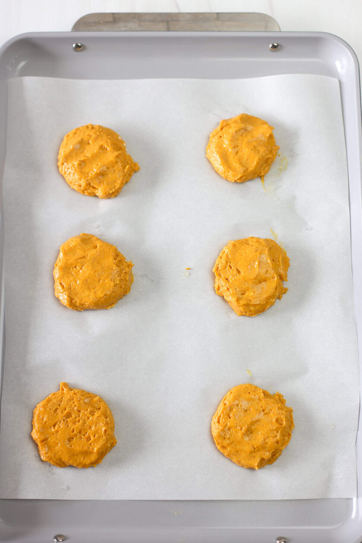 Pumpkin spice cake mix cookie batter in scoops on a parchment-lined baking sheet.