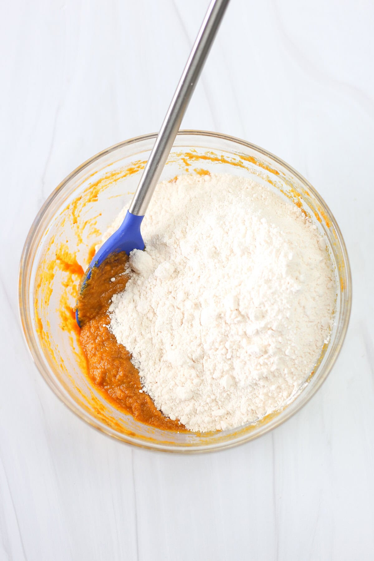 Pumpkin puree in a mixing bowl with yellow cake mix being mixed in.