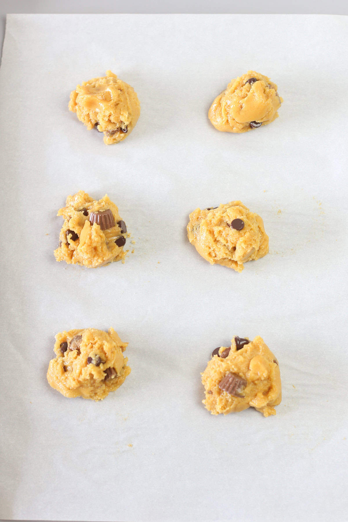 Reese's peanut butter cup cake mix cookie dough balls on a parchment paper lined baking sheet ready for the oven.