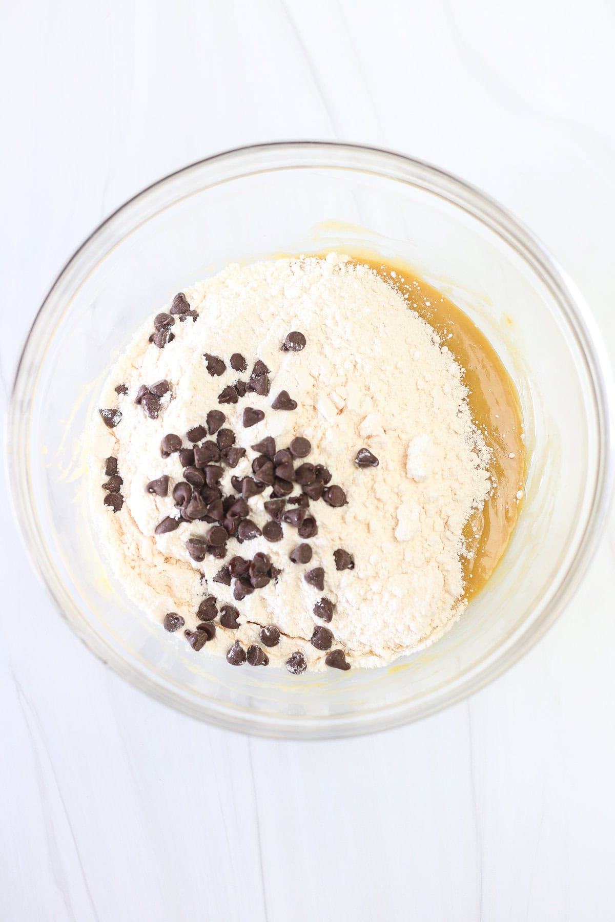 Glass bowl with cake mix and chocolate chips being mixed into wet ingredients for Reese's peanut butter cup cake mix cookies.