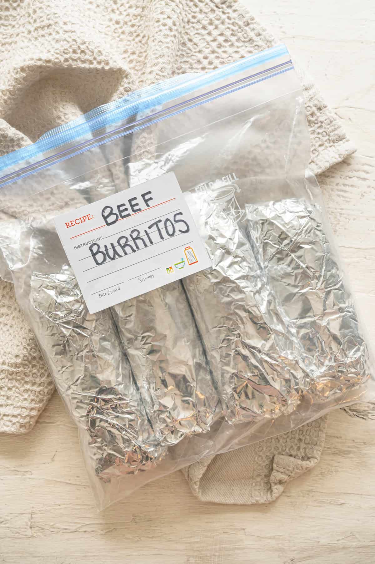 A gallon-size freezer bag labeled beef burritos with four burritos wrapped in foil inside.