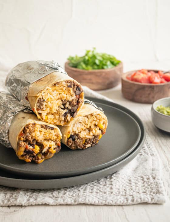 Three beef burrito halves wrapped in foil halfway stacked up on a plate.